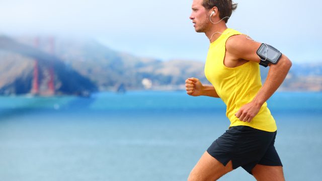 man in bright yellow tank sprints by water